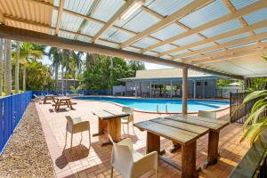 patio con mesa de madera, sillas y piscina en Kondari Hotel, en Hervey Bay