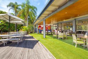 un patio al aire libre con mesas, sillas y una sombrilla en Kondari Hotel en Hervey Bay