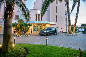 a car parked in front of a building with palm trees at Hotel Isola Sacra Rome Airport in Fiumicino