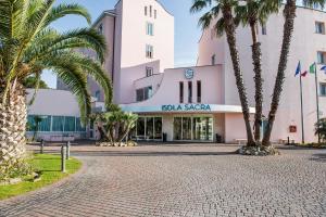 a pink building with palm trees in front of it at Hotel Isola Sacra Rome Airport in Fiumicino
