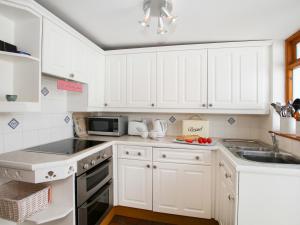 a white kitchen with white cabinets and a sink at Gorffwysfa in Valley