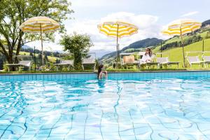 a girl in a swimming pool with umbrellas at Hotel Tyrol in Funes