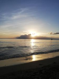 a sunset on the beach with a boat in the water at Maison Duplex "Josué" vue sur Marina in Grand-Bourg