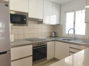 cocina con armarios blancos, fregadero y microondas en Sunny & New Apartamento in Caleta de Fuste, en Caleta de Fuste