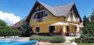 a yellow house with an umbrella next to a pool at Schieszl Apartments Zamárdi 1 in Zamárdi