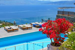 a pool with tables and red flowers next to the water at Villa Olga in Agios Nikolaos