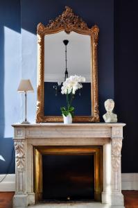 un espejo sobre una chimenea con un jarrón de flores. en Romance au coeur de Bordeaux / Jardin Public, en Burdeos