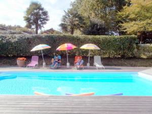 Maison Canterou في Monein: مجموعة من الناس يجلسون تحت المظلات بجوار حمام السباحة
