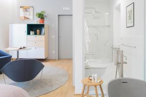 a white bedroom with a blue chair and a bathroom at The Radical Hotel Roma in Rome