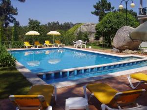 a swimming pool with chairs and umbrellas in a yard at Hotel & Apartamentos Cons da Garda in San Vicente de O Grove
