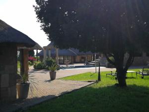 a park with a tree and benches and a building at Stone Hounds Lodge in Magaliesburg