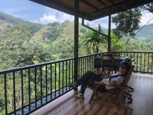 uma mulher sentada numa cadeira num alpendre com vista em Green Village em Ella