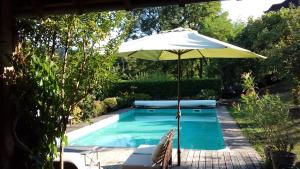 a pool with an umbrella and a chair and a table at Les Perluètes - Chambres d'hôtes in Carennac