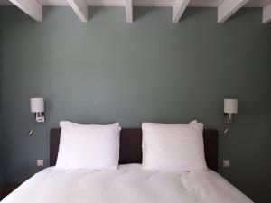 a bed with two white pillows and two lights on the wall at Lodges near the Rhine - Sustainable Residence in Hazerswoude-Rijndijk