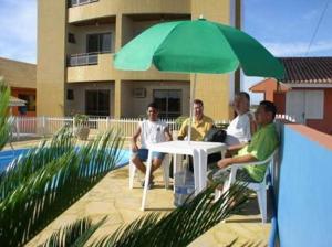 um grupo de homens sentados à volta de uma mesa sob um guarda-chuva verde em Hotel Pousada Mineirinho em Balneário Praia do Leste