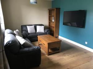 a living room with a black leather couch and a tv at Heb Holiday, Self Catering Accommodation, Isle of Benbecula in Gramisdale