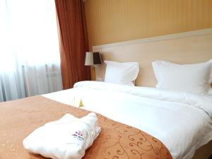 2 camas en una habitación de hotel con sábanas y almohadas blancas en King Hotel Astana en Astaná
