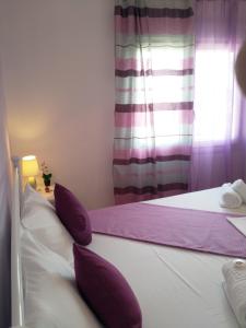 una camera con 2 letti con cuscini viola e finestra di Nikoletta Rooms a Paroikia