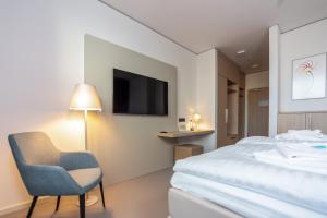 a bedroom with a bed and a chair and a tv at Hotel Vivendi in Paderborn