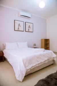 a white bedroom with a large bed with white sheets at MC Apartments in Lusaka