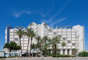a large white building with palm trees in front of it at King Solomon Hotel Tiberias in Tiberias