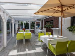 eine Terrasse mit Tischen, Stühlen und einem Sonnenschirm in der Unterkunft Apartments Herrlichkeit Dornum in Dornum