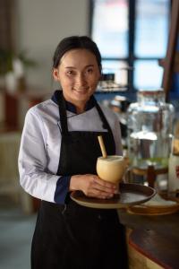 une femme tient une assiette avec une boisson dans l'établissement Indigo House Hotel, à Luang Prabang