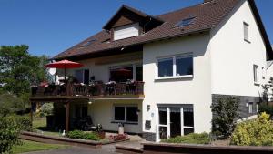 een wit huis met een balkon met een parasol bij Ferienwohnung am Lieserpfad in Nerdlen