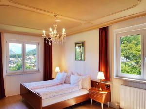 a bedroom with a bed with two windows and a chandelier at Aparthotel Pan Haus in Bad Ischl