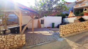a building with a tree and a stone wall at Apartments Niko Metajna, island Pag in Metajna