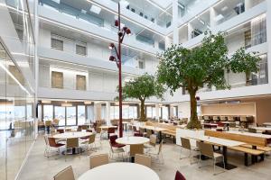 eine Cafeteria mit Tischen und Bäumen in einem Gebäude in der Unterkunft Hotel Vivendi in Paderborn