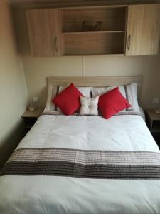 a large bed with red and white pillows on it at Private Caravan on Golden Sands Holiday Park, North Wales in Foryd