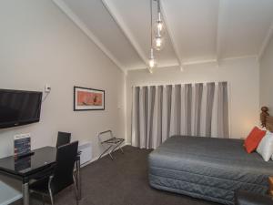a bedroom with a bed and a desk and a tv at Cedar Lodge Motel in Timaru