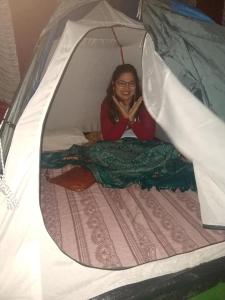 una mujer sentada en una cama en una tienda en coorg camping tent stay, en Suntikoppa
