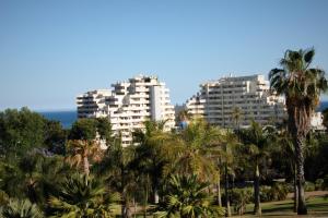 dwa wysokie białe budynki z palmami i oceanem w obiekcie Benalbeach w mieście Benalmádena
