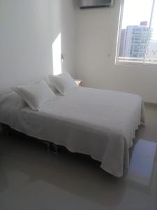 Cama blanca en habitación con ventana en Apartamentos Reserva del Mar, en Santa Marta