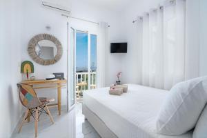 a white bedroom with a bed and a desk and a window at Central Suites Mykonos in Mýkonos City