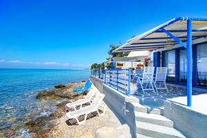 a porch with chairs and tables and the ocean at GLAROS BUNGALOW in Skala Kallirachis