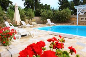 a swimming pool with white chairs and red flowers at BUNGALOW VICE with pool in Pakoštane