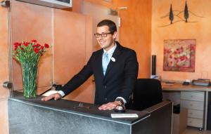 Un uomo in giacca e cravatta alla scrivania con un vaso di fiori di Hotel La Colonna a Siena