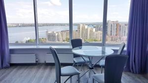 una mesa y sillas en una habitación con ventanas grandes en Most City Apart-Hotel, en Dnipro