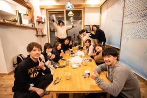een groep mensen die rond een tafel zitten bij Katsuo Guest House in Kochi