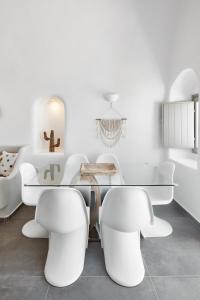 uma sala de jantar com uma mesa de vidro e cadeiras brancas em Mellow Luxury Cave em Oia