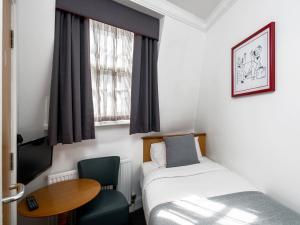 Cette petite chambre comprend un lit et une table. dans l'établissement OYO Townhouse New England, London Victoria, à Londres