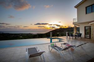 a patio with chairs and a pool with a sunset at Villa Blue Jadeite in Peyia