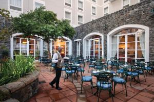 un uomo in piedi di fronte a un patio con tavoli e sedie di The Commodore Hotel a Città del Capo