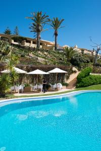 a person standing next to a swimming pool with palm trees at Vila Joya in Albufeira