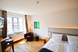 a hotel room with a bed and a chair and a window at Qube Hotel Bergheim in Heidelberg