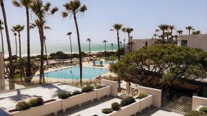 a view of a pool with palm trees and the ocean at Hipotels Barrosa Park in Chiclana de la Frontera