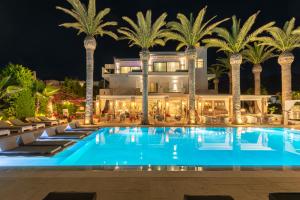 a hotel with a pool and palm trees at night at Drossia Palms Hotel and Nisos Beach Suites in Malia